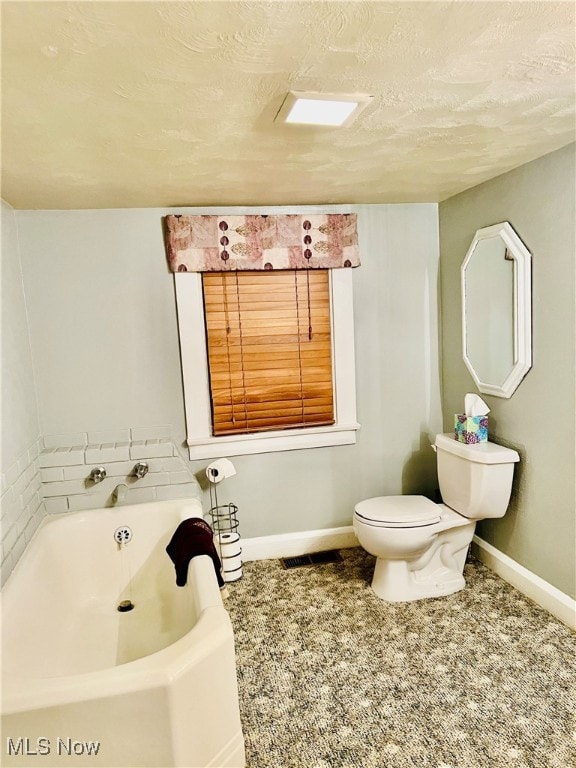 bathroom with a bathing tub, a textured ceiling, and toilet