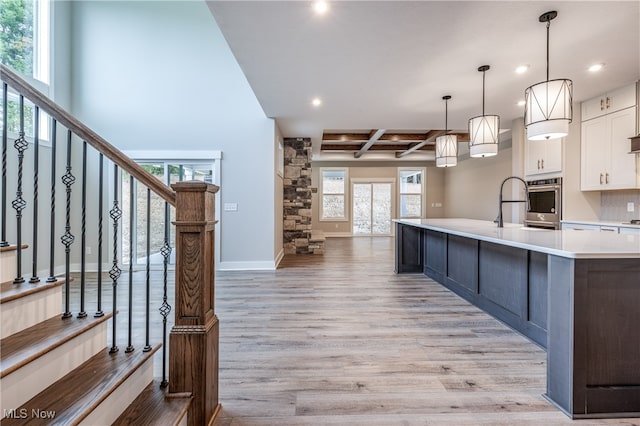 kitchen featuring decorative light fixtures, white cabinets, a large island, coffered ceiling, and light hardwood / wood-style flooring