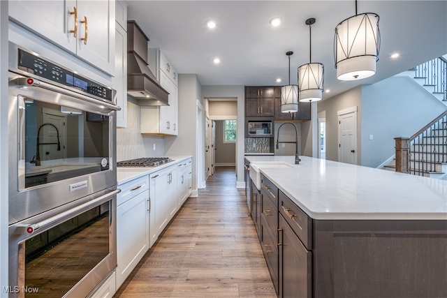 kitchen with appliances with stainless steel finishes, decorative light fixtures, a center island with sink, and white cabinets