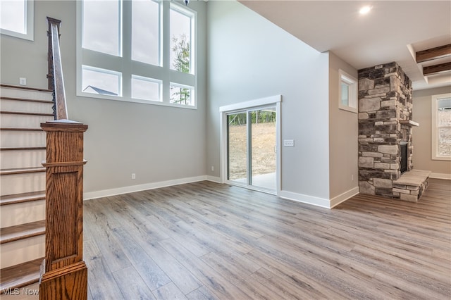 unfurnished living room with a stone fireplace, light hardwood / wood-style floors, and a high ceiling