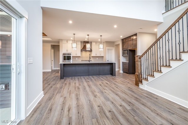 kitchen featuring light hardwood / wood-style floors, a kitchen island with sink, tasteful backsplash, custom range hood, and stainless steel appliances