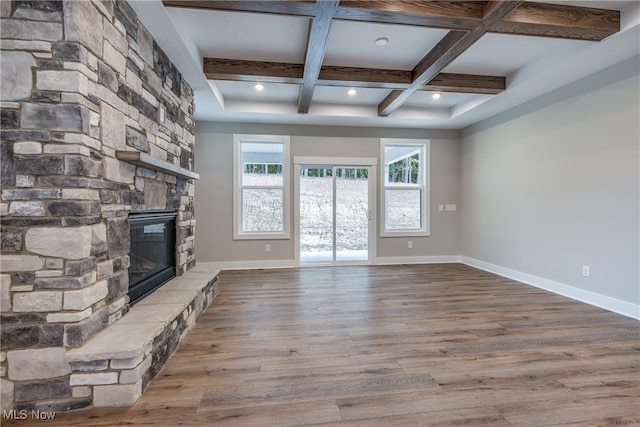 unfurnished living room with beamed ceiling, coffered ceiling, a stone fireplace, and wood-type flooring