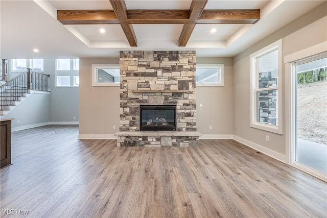 unfurnished living room with coffered ceiling, a stone fireplace, light hardwood / wood-style floors, and beamed ceiling