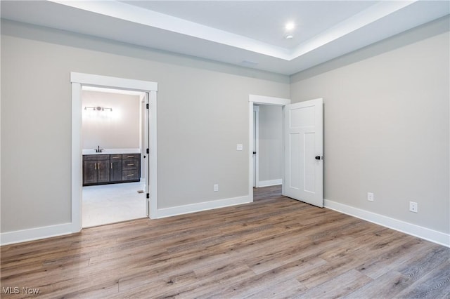 unfurnished bedroom with sink, connected bathroom, a raised ceiling, and light hardwood / wood-style floors