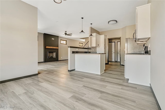 kitchen featuring ceiling fan, white cabinets, kitchen peninsula, decorative light fixtures, and a large fireplace