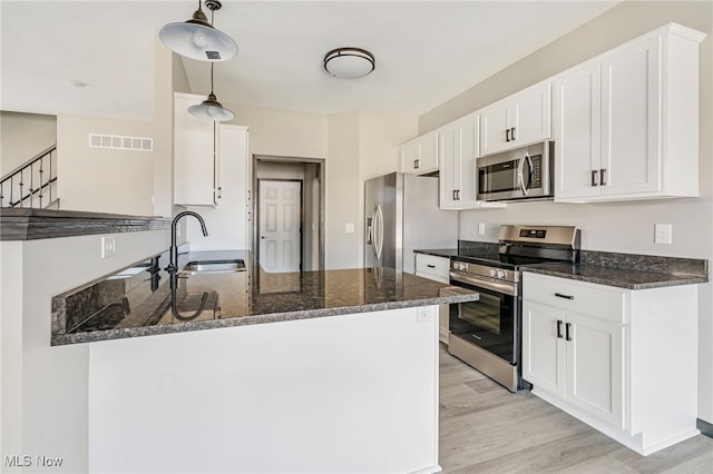 kitchen with white cabinets, sink, appliances with stainless steel finishes, dark stone countertops, and light hardwood / wood-style floors