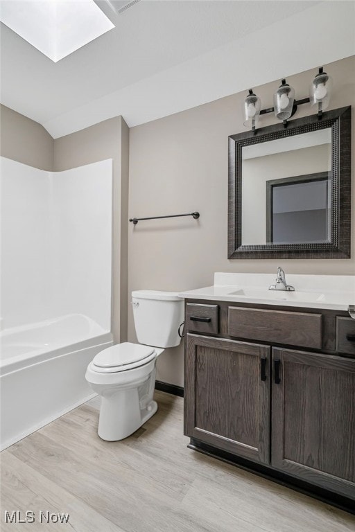 full bathroom with bathtub / shower combination, wood-type flooring, a skylight, vanity, and toilet