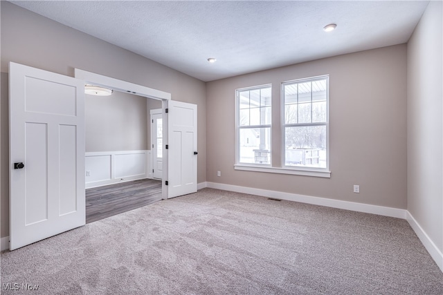 carpeted spare room featuring a textured ceiling, visible vents, and baseboards