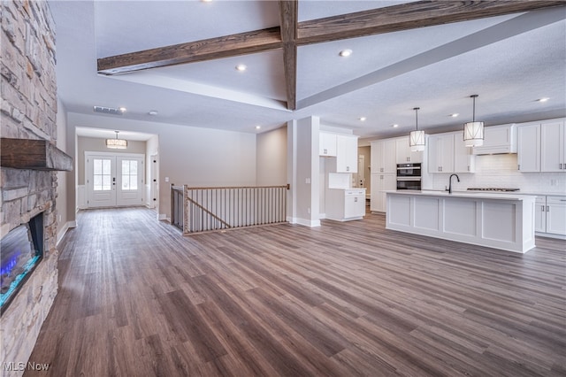 unfurnished living room featuring dark wood-style floors, french doors, a sink, and beamed ceiling