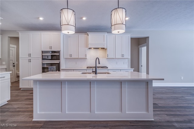 kitchen with hanging light fixtures, light stone counters, and a center island with sink