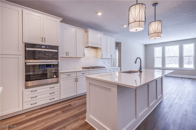 kitchen featuring hanging light fixtures, a kitchen island with sink, white cabinets, and a sink