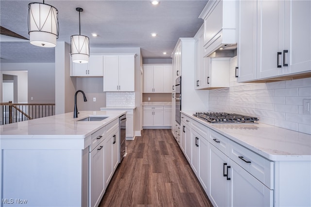 kitchen featuring pendant lighting, stainless steel appliances, a kitchen island with sink, white cabinetry, and a sink