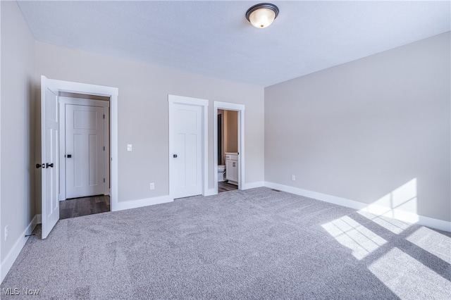 unfurnished bedroom with dark colored carpet, connected bathroom, and baseboards