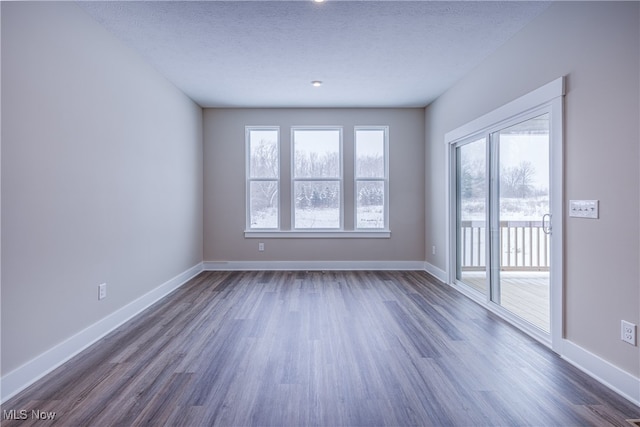 empty room featuring a textured ceiling, dark wood finished floors, and baseboards