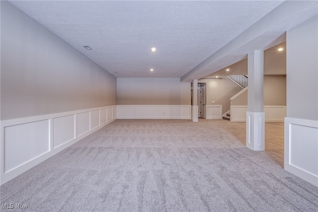 finished basement with light carpet, visible vents, a wainscoted wall, stairs, and a textured ceiling