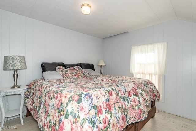 bedroom with light hardwood / wood-style flooring, wooden walls, and lofted ceiling