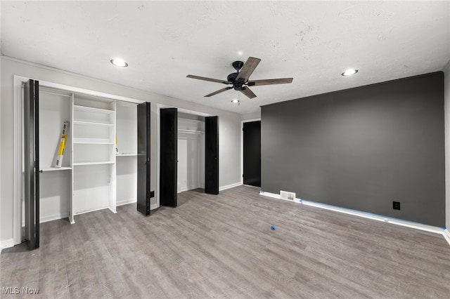 unfurnished bedroom with a textured ceiling, ceiling fan, multiple closets, and hardwood / wood-style flooring