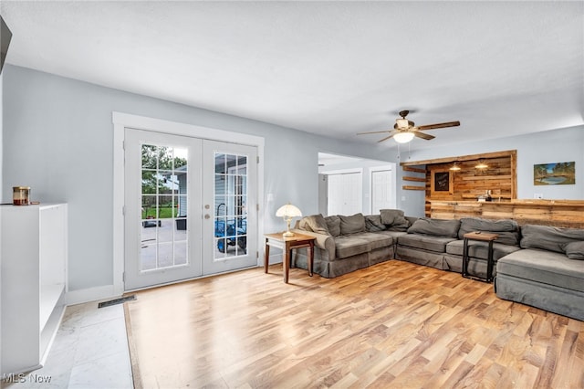 living room featuring wooden walls, french doors, ceiling fan, and light hardwood / wood-style flooring