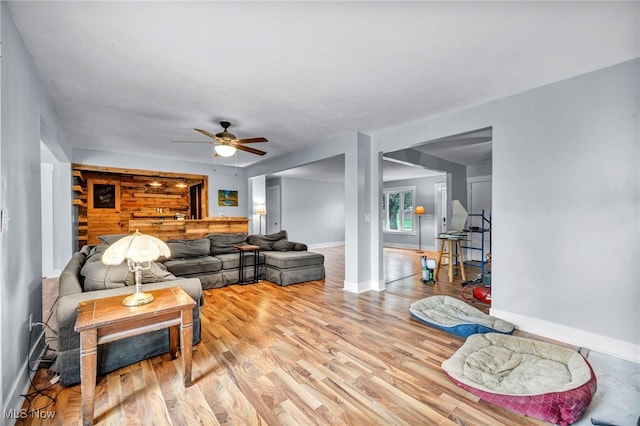 living room with light hardwood / wood-style floors, wooden walls, and ceiling fan