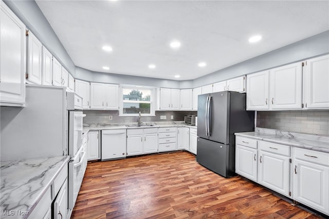 kitchen with stainless steel refrigerator, white cabinetry, sink, white dishwasher, and light wood-type flooring