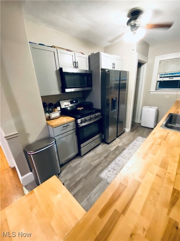 kitchen featuring light wood-type flooring, gray cabinetry, appliances with stainless steel finishes, wooden counters, and ceiling fan