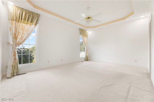 unfurnished room with ceiling fan, a raised ceiling, and light carpet