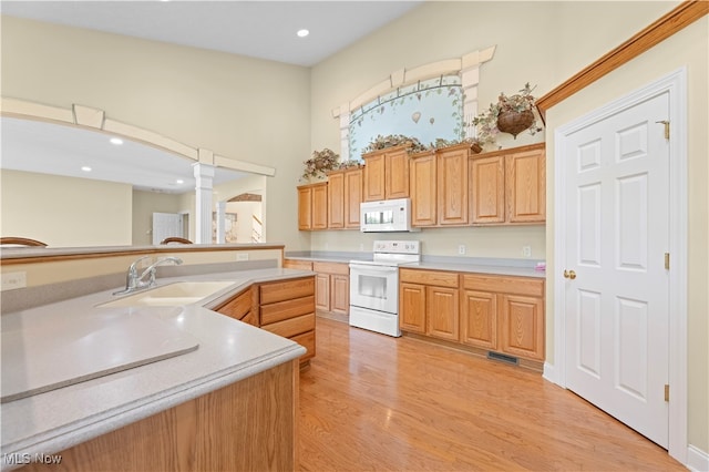 kitchen with decorative columns, white appliances, light hardwood / wood-style floors, and sink