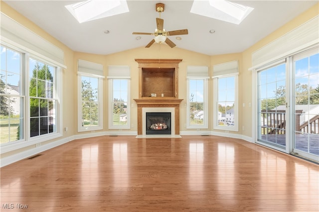 unfurnished living room featuring light wood-type flooring, a premium fireplace, lofted ceiling with skylight, and ceiling fan