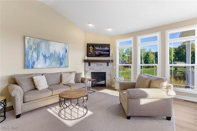 living room featuring vaulted ceiling, plenty of natural light, and a stone fireplace