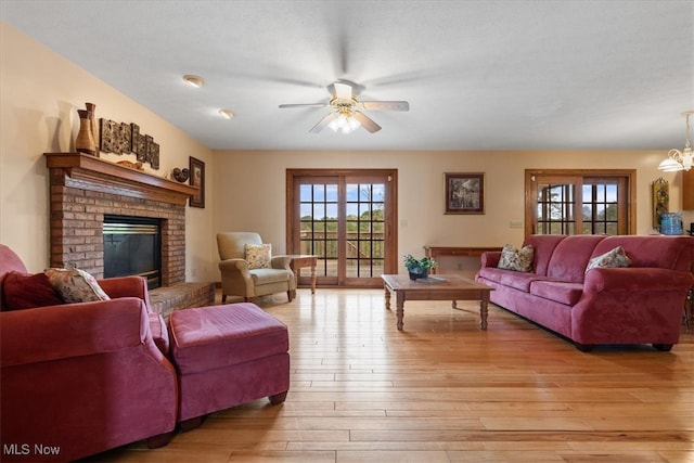 living room featuring light wood-type flooring, a brick fireplace, and ceiling fan