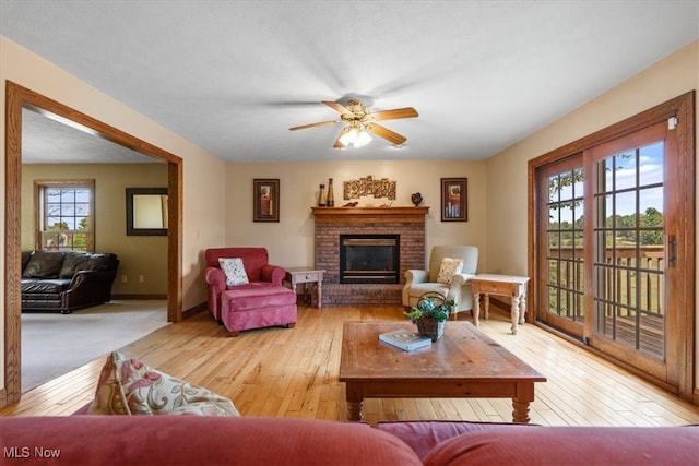 living room with a brick fireplace, light hardwood / wood-style flooring, and ceiling fan