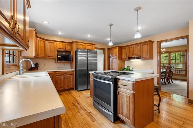 kitchen with appliances with stainless steel finishes, sink, light hardwood / wood-style flooring, a center island, and hanging light fixtures