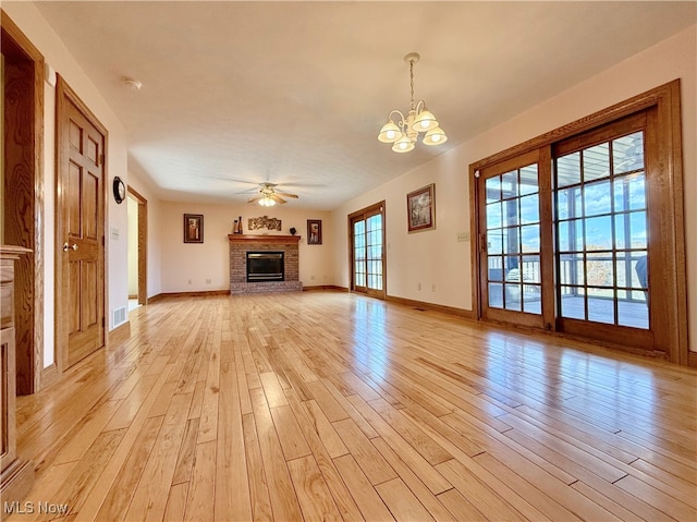 unfurnished living room featuring ceiling fan with notable chandelier, light wood-type flooring, and a fireplace