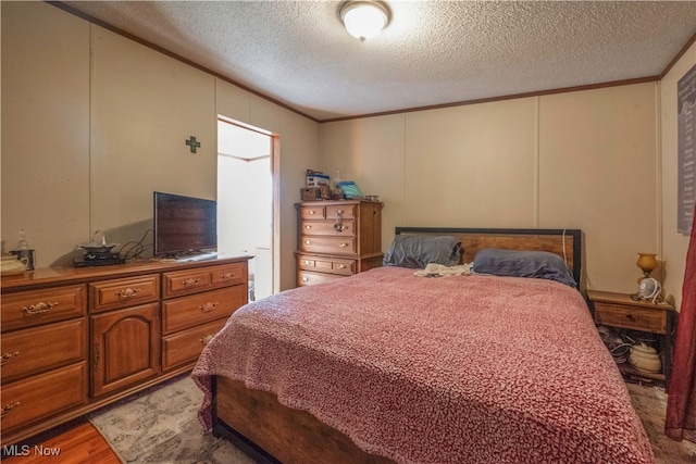 bedroom with a textured ceiling, light wood-type flooring, and crown molding