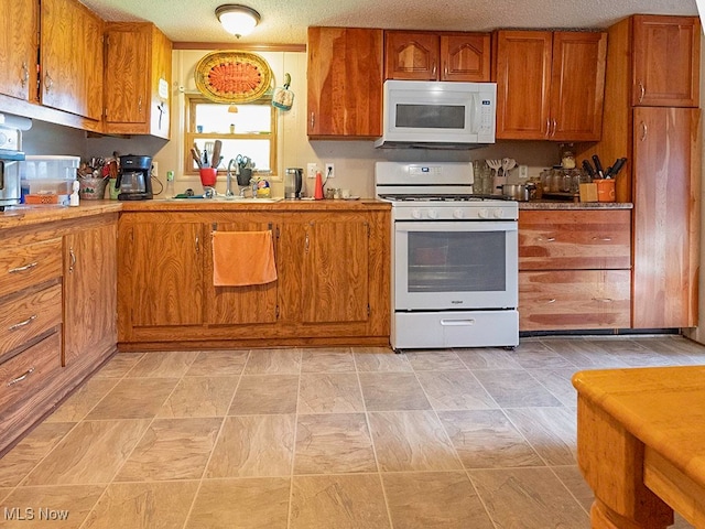 kitchen featuring white appliances, a textured ceiling, and sink