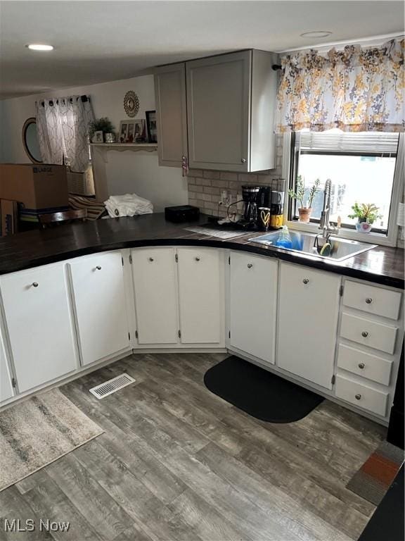9151 Mentor Ave Unit A14, Mentor, OH 44060 - kitchen with dark countertops, visible vents, decorative backsplash, a sink, and wood finished floors