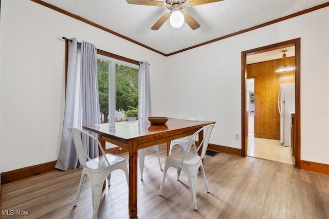 dining room featuring light hardwood / wood-style flooring, wooden walls, ceiling fan, and ornamental molding