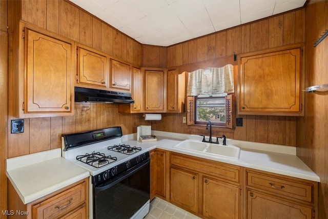 kitchen featuring wood walls, white range with gas cooktop, and sink