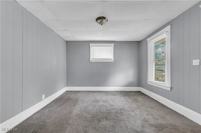 unfurnished room featuring a drop ceiling, wood walls, and carpet flooring