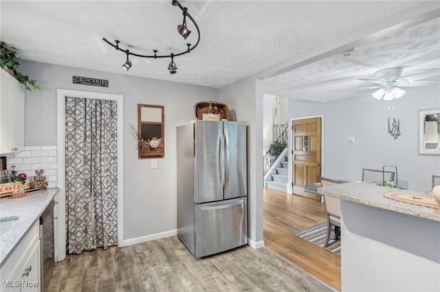 kitchen with a textured ceiling, appliances with stainless steel finishes, light wood-type flooring, and white cabinetry