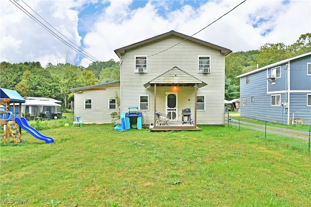 back of house featuring a lawn, a wooden deck, and a playground