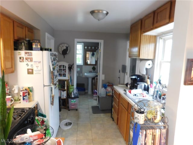 kitchen featuring light tile patterned floors, white refrigerator, sink, and a wealth of natural light