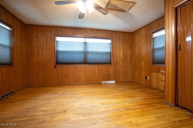 empty room with light wood-type flooring, wood walls, ceiling fan, and plenty of natural light