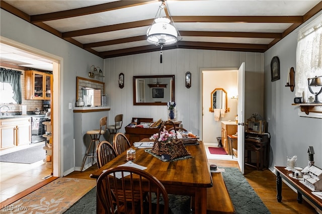 dining area featuring a healthy amount of sunlight, light hardwood / wood-style floors, lofted ceiling with beams, and wood walls