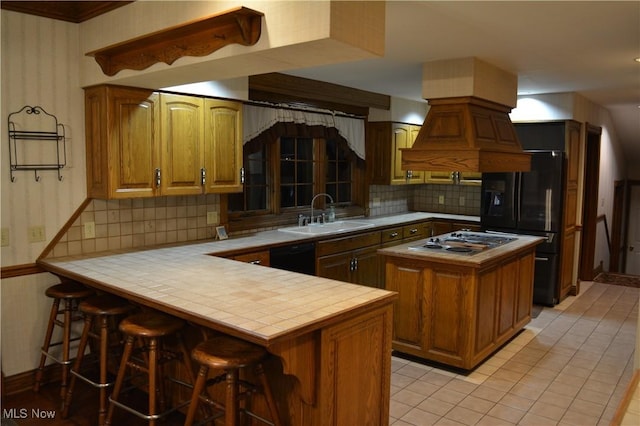 kitchen with sink, tile countertops, kitchen peninsula, a breakfast bar area, and black appliances