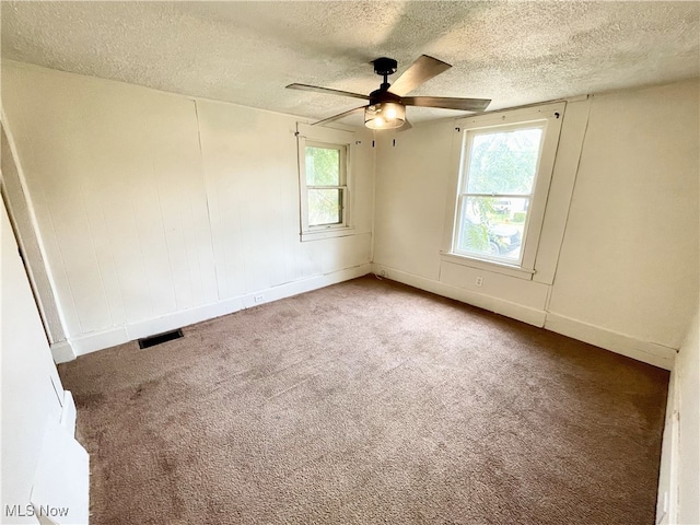 carpeted empty room featuring ceiling fan, a textured ceiling, and a wealth of natural light