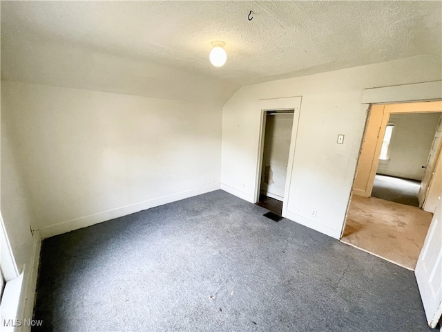 unfurnished bedroom with carpet, a closet, lofted ceiling, and a textured ceiling