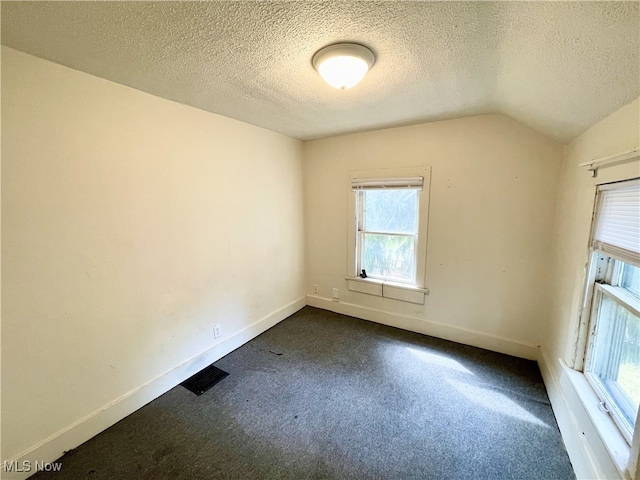 carpeted spare room featuring a textured ceiling and vaulted ceiling