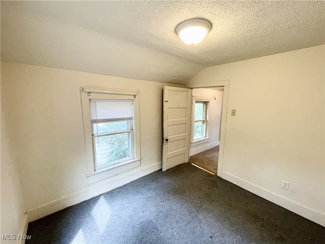 unfurnished bedroom featuring dark carpet, vaulted ceiling, multiple windows, and a textured ceiling