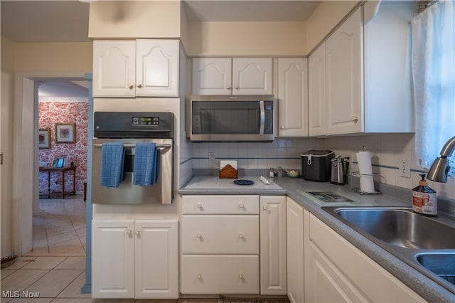 kitchen featuring backsplash, white cabinets, sink, light tile patterned floors, and appliances with stainless steel finishes